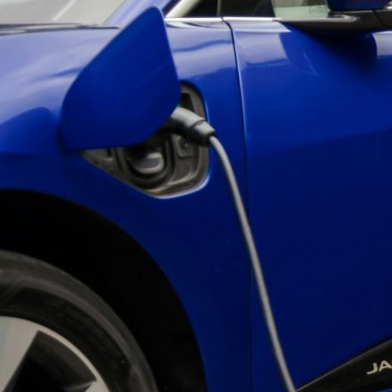 Blue electric vehicle (EV) charging using a portable EV charger, connected to the charging port on the side of the car.